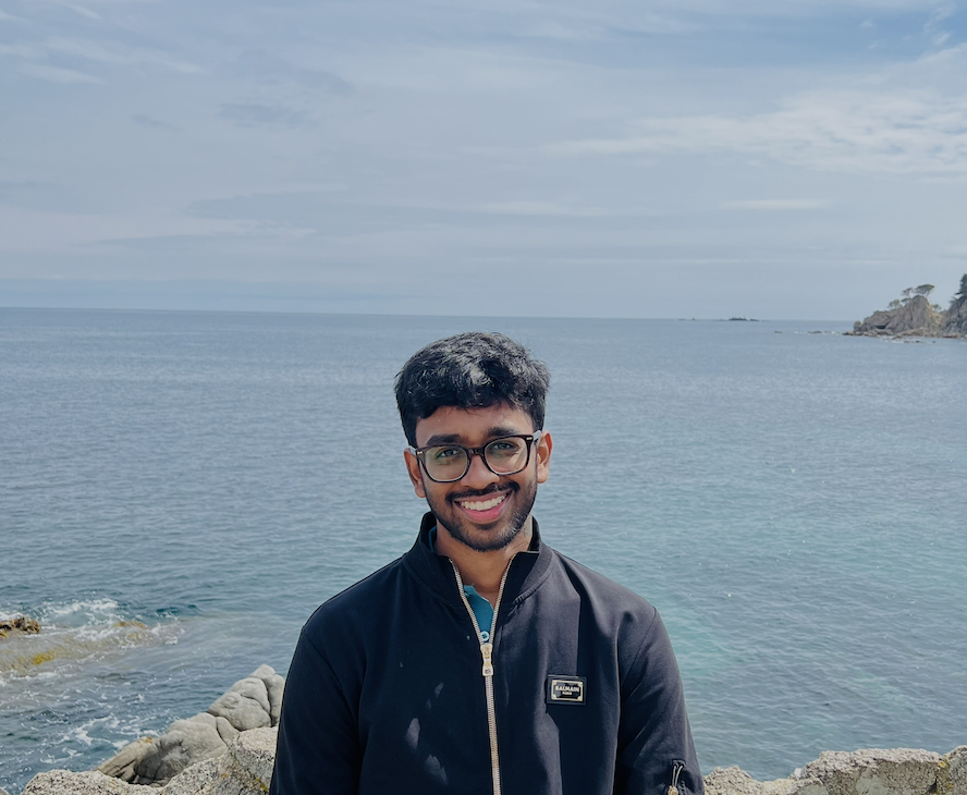 Ajay Ennarasu standing by the sea, smiling